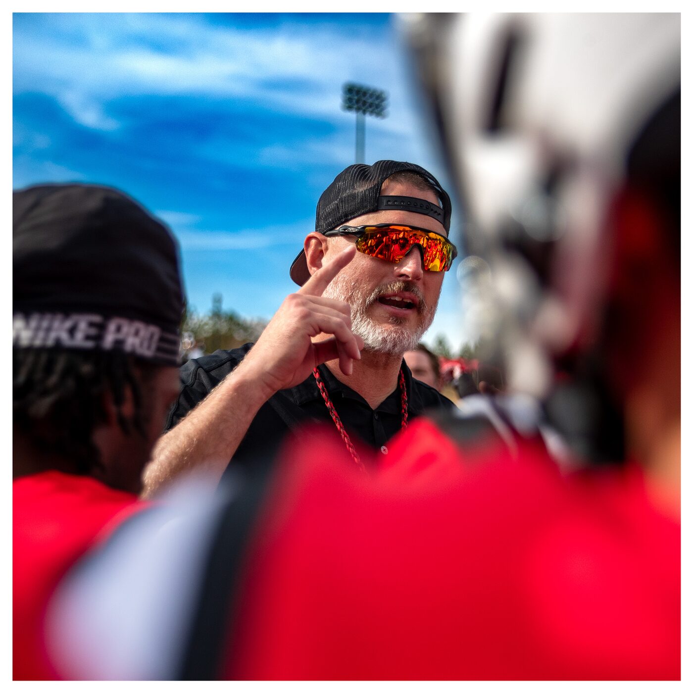 Coach Garner in a player huddle, mid-instruction, under a bright sky.