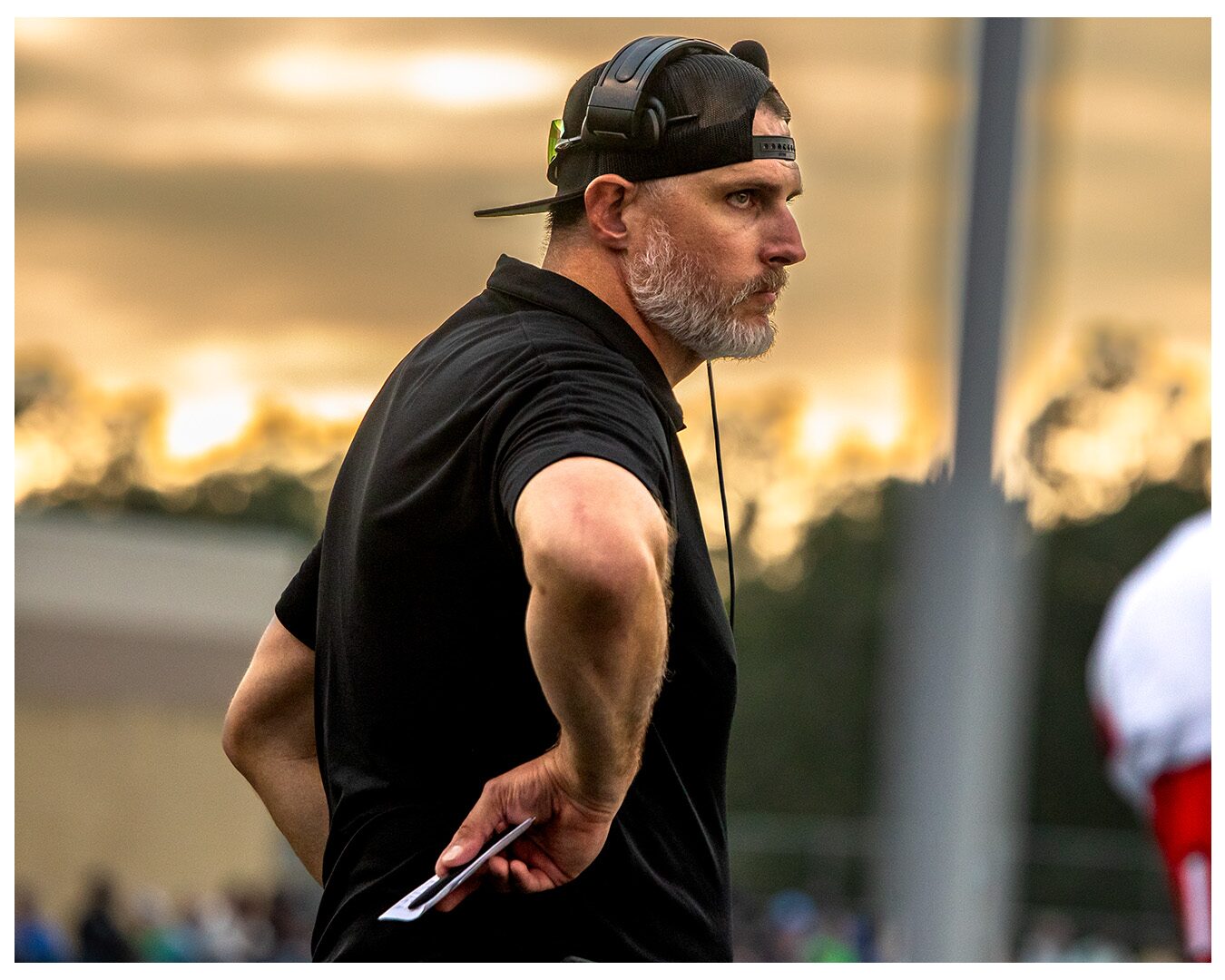 Coach Nate Garner on the sideline at sunset, eyes on the field.